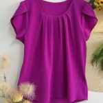 Blusa Plus Size Laís em rosê, com mangas curtas de pétala, gola redonda, bainha flared e detalhes dobrados. Confortável e elegante para o dia a dia.
