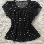 Blusa Plus Size Fernanda com estampa de bolinhas poá, fundo preto, mangas pétala, gola redonda. Confortável, clássica e versátil.