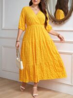 Vestido Plus Size Amanda em rosa chiclete, design em A, cintura alta, mangas bishop, decote V, babados esvoaçantes e detalhes cruzados.