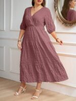 Vestido Plus Size Amanda em rosa chiclete, design em A, cintura alta, mangas bishop, decote V, babados esvoaçantes e detalhes cruzados.