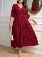 Vestido Plus Size Amanda em rosa chiclete, design em A, cintura alta, mangas bishop, decote V, babados esvoaçantes e detalhes cruzados.